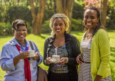 Three women smiling while holding coffee cups.